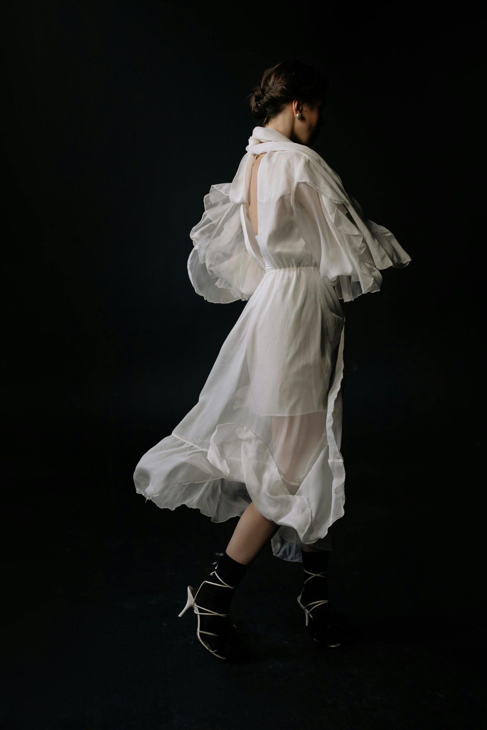 Artistic studio shot of a woman in a flowing sheer white dress with a dark background.